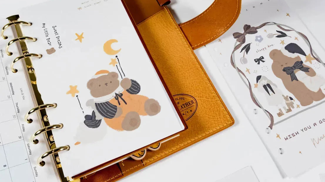Miouva planner divider pages with teddy bear illustration inside a brown leather Filofax-style binder - gentle and cozy design for planners and journaling.